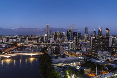 Aerial view of Brisbane CBD skyline at blue hour with illuminated Story Bridge and Brisbane River below.