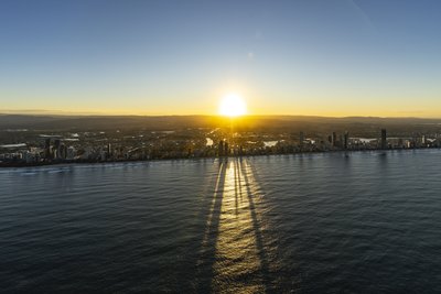 Aerial view of the Gold Coast skyline at sunset, with dramatic building shadows stretching across the Pacific Ocean.