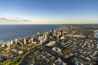 Aerial view of Surfers Paradise skyline at golden hour with canal suburbs and Nerang River below.