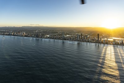 Helicopter aerial of the Gold Coast coastal strip at sunrise with hinterland ranges behind.