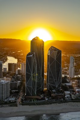 Aerial view of the Gold Coast's Surfers Paradise, featuring angular high-rise towers silhouetted against a golden sunset with the Broadwater in the background.