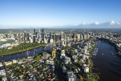 Aerial view of Brisbane CBD and Kangaroo Point cliffs in warm morning light, with lush parklands along the river.