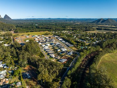 Aerial view of a residential estate amid lush countryside with the Glass House Mountains beyond.
