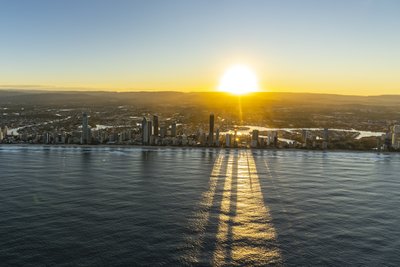Aerial view of the Gold Coast at sunrise, showcasing Surfers Paradise towers casting long shadows on the ocean.