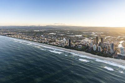 Aerial view of the Gold Coast coastline at sunrise with rolling surf and canal suburbs behind.