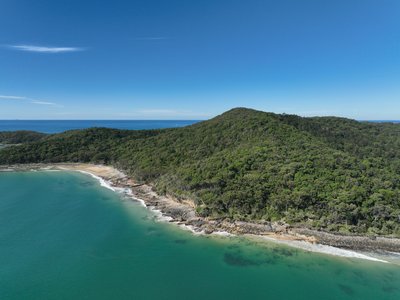 Aerial drone shot of Noosa Heads coastline with thick native vegetation, rocky cliffs and clear turquoise waters.