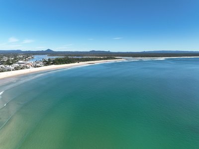 High altitude aerial of Noosa Main Beach and Noosa Spit looking north, showing the full bay, national park and Sunshine Coast hinterland.