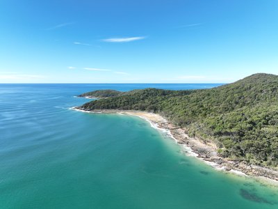 Aerial view of Noosa National Park coastline with forested headland peaks, rocky shoreline and clear turquoise waters.