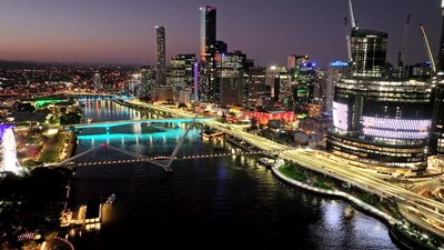 Aerial night view of Brisbane CBD skyline with illuminated bridges and Brisbane River below.