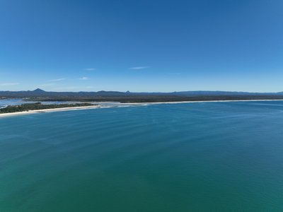 A high altitude aerial view of Laguna Bay, showcasing the sand spit and coastline with Glass House Mountains in the distance.
