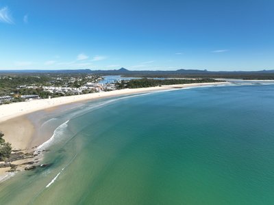A higher altitude aerial view of Noosa Main Beach and town, with the Noosa River mouth visible in the background.