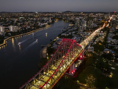 Aerial view of illuminated Story Bridge at night with Brisbane River and surrounding suburbs in Queensland, Australia.