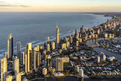 Aerial view of Surfers Paradise towers at golden hour with Nerang River waterways and beach beyond.