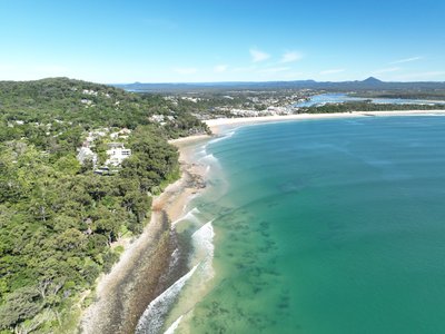 Aerial view of Noosa with rocky headland foreground, Main Beach and town visible in the mid-distance.