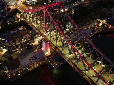 Close overhead night aerial of Story Bridge with red illumination and Felons Brewing Co visible.