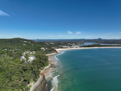 High aerial view of Noosa from the ocean showing Main Beach, town and hinterland panorama.