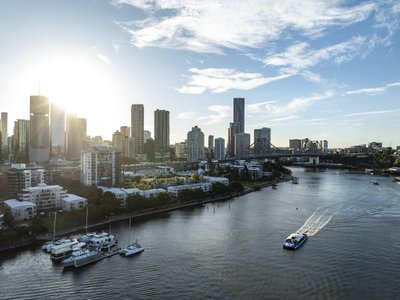 Aerial view of Brisbane's New Farm Riverwalk, featuring the Story Bridge and CBD skyline during a morning golden hour.