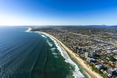 Aerial view of Coolangatta beach and coastline with the Gold Coast hinterland mountains in the background.