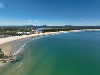 A wide aerial panorama of Noosa Main Beach, including the township and surrounding natural features.