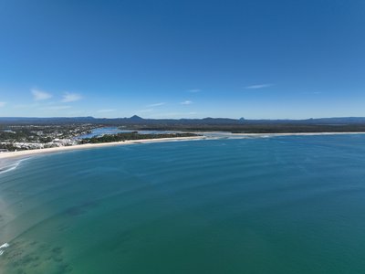 A wide panoramic aerial view of Noosa and the Sunshine Coast hinterland, showcasing Main Beach, river estuary, Glass House Mountains.