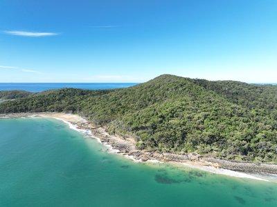 Aerial view of Noosa Heads' headland where dense rainforest meets the rocky Pacific coastline with turquoise inshore waters.