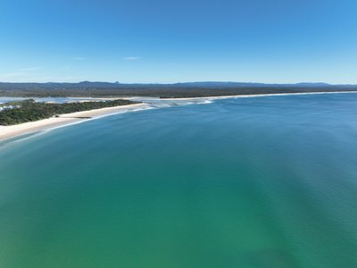 A high altitude aerial view over Laguna Bay with Noosa Spit, beach and national park visible. The open Pacific Ocean dominates the frame.