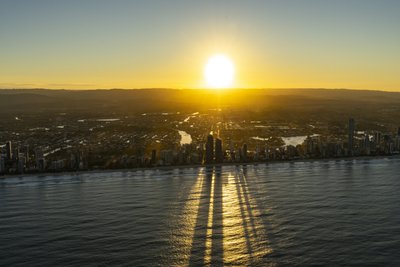 Dramatic sunrise aerial with Surfers Paradise towers casting long shadows across ocean from offshore.