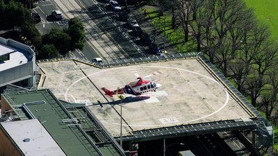 Aerial view of a helicopter ambulance on the rooftop hospital helipad, surrounded by streets and park in Brisbane City.