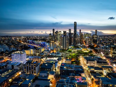 Aerial view of Brisbane's CBD at dusk, featuring the Story Bridge and vibrant city lights along the river.