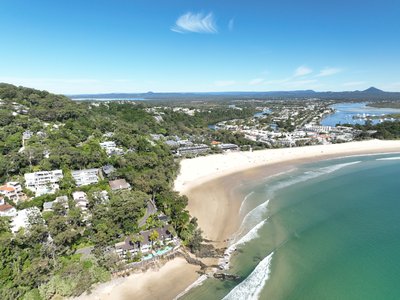 A drone view from Noosa Heads headland looking south along Main Beach with the Noosa township and Noosa River in the background.