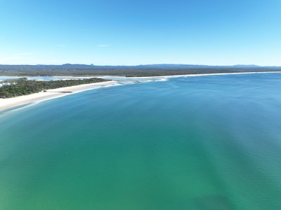A high drone view over Laguna Bay with Noosa Spit and coastline visible to the left, and the Sunshine Coast hinterland in the distance.