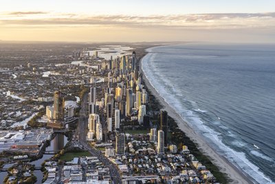 Aerial view of the Gold Coast coastal strip at sunrise, featuring Surfers Paradise towers and a long sandy beach stretching north.