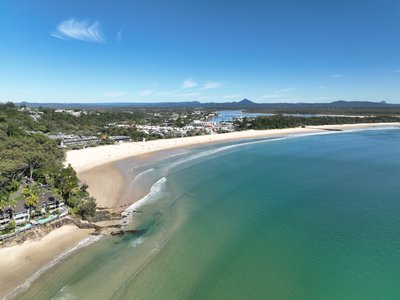 Aerial view of Noosa Main Beach curving south with the Noosa township, Noosa River mouth and Glass House Mountains in the background.