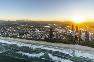 Low aerial from offshore of Broadbeach at golden hour with waves and Gold Coast skyline beyond.