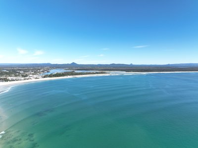 A high altitude aerial overview of Noosa with Main Beach, Noosa River, and the Glass House Mountains visible.