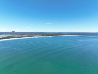Aerial overview of Laguna Bay and Noosa Spit from high altitude with the Glass House Mountains visible across the hinterland.