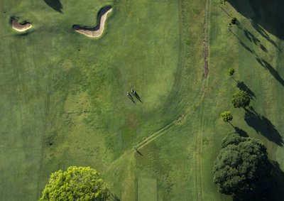 Near-vertical aerial view of a golf course fairway with sand bunkers and golfers visible below.