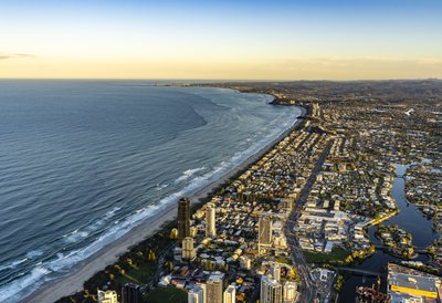 Aerial view of the Gold Coast coastline with Surfers Paradise in sight, featuring canal suburbs and ocean waves.