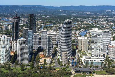 Aerial view of the Gold Coast Broadbeach area, showcasing distinctive curved high-rise towers and a river backdrop.