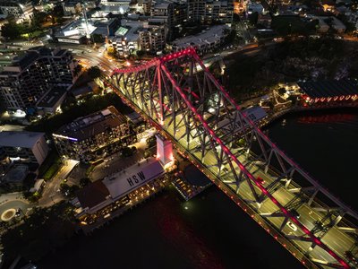 Overhead night aerial of Story Bridge with red LED lighting and Howard Smith Wharves below.
