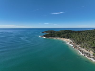 Aerial drone shot of Noosa National Park coastline featuring rocky cliffs, native rainforest and a hidden sandy cove.
