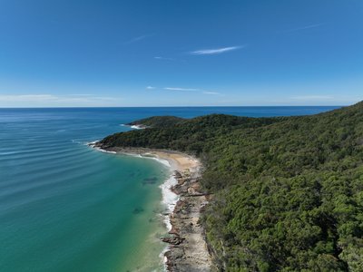 Aerial drone shot of a secluded beach cove in Noosa National Park, featuring rocky headlands and native rainforest.