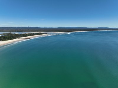 Elevated aerial of Laguna Bay showing the Noosa Spit sand bar, national park coastline and vast turquoise waters of the Pacific Ocean.