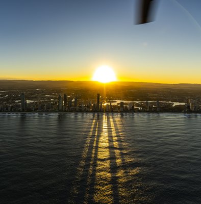 Aerial helicopter view of Gold Coast skyscrapers silhouetted against a vivid sunset over the ocean.
