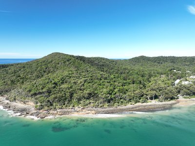 Aerial view of Noosa Heads coastline, featuring forested headlands and rocky shoreline.