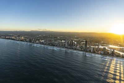 Aerial view of the Gold Coast coastline at sunrise, featuring a skyline with high-rise buildings and the ocean in the foreground.