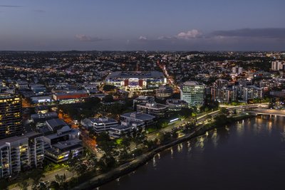 Aerial dusk view of Brisbane Suncorp Stadium lit up beside the Brisbane River with city lights.