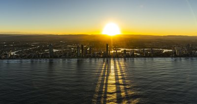 Aerial sunrise view of Gold Coast skyline with long building shadows reaching across ocean.
