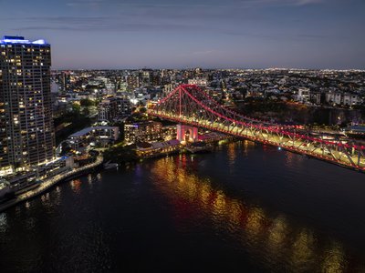 Aerial view of Story Bridge illuminated with red LED lighting at night reflecting in the Brisbane River.
