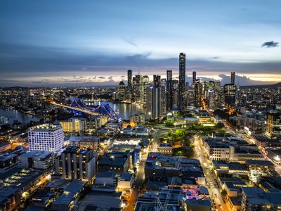 Aerial view of Brisbane CBD at dusk with illuminated Story Bridge and city skyline reflected in the river.